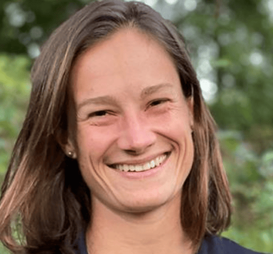 Dr. Alexandra Uden smiling outdoors with a blurred green background of trees and foliage.