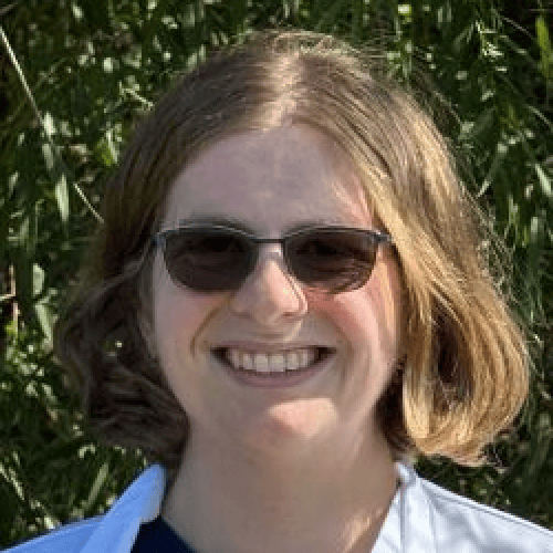 Dr. Angela Feiring smiling outdoors in a white coat and sunglasses, with greenery in the background.