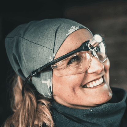 Smiling woman wearing a headlamp, safety glasses, and a headscarf, prepared for equine veterinary work.