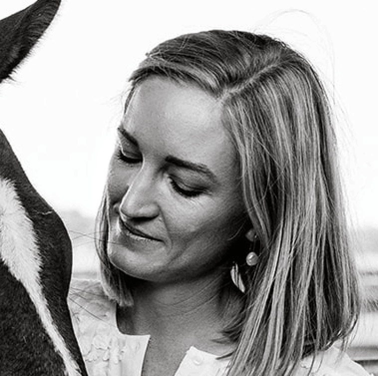 Woman smiling affectionately at a horse in a close-up black and white portrait.