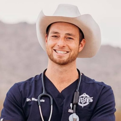 Smiling male veterinarian in cowboy hat and navy scrubs with stethoscope around his neck